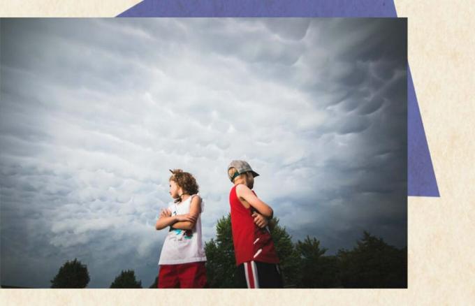 αδερφός και αδερφή ντυμένοι στα ερυθρόλευκα με τις πλάτες τους αντικριστά κάτω από έναν συννεφιασμένο ουρανό