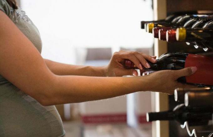nėščia moteris griebia vyno butelį