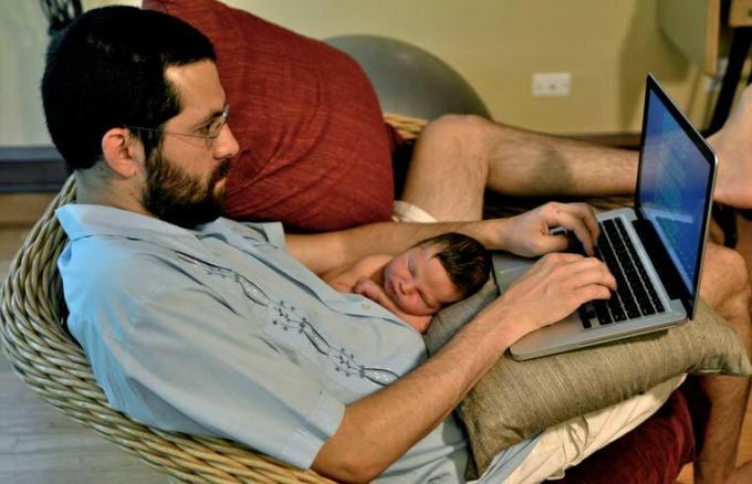 táta na počítači, zatímco drží dítě