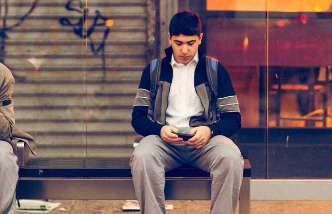 έφηβος που χρησιμοποιεί το τηλέφωνο στη στάση του λεωφορείου