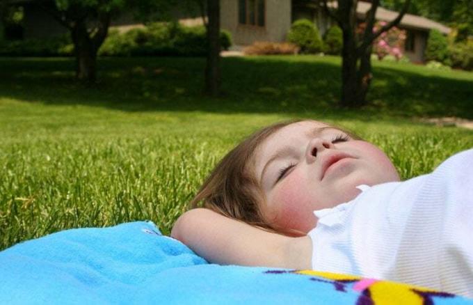 პატარა ბავშვი გაზონზე მზის აბაზანების მისაღებად